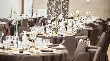 Un salón de banquetes con mesas dispuestas para un evento formal, con tarjetas de identificación numeradas y centros de mesa con flores.