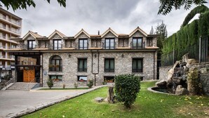 Un edificio de piedra con fachada simétrica, varias ventanas y un pequeño jardín con una fuente.