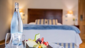 Una habitación de hotel con una cama, una botella de agua y una bandeja de frutas sobre una mesa.
