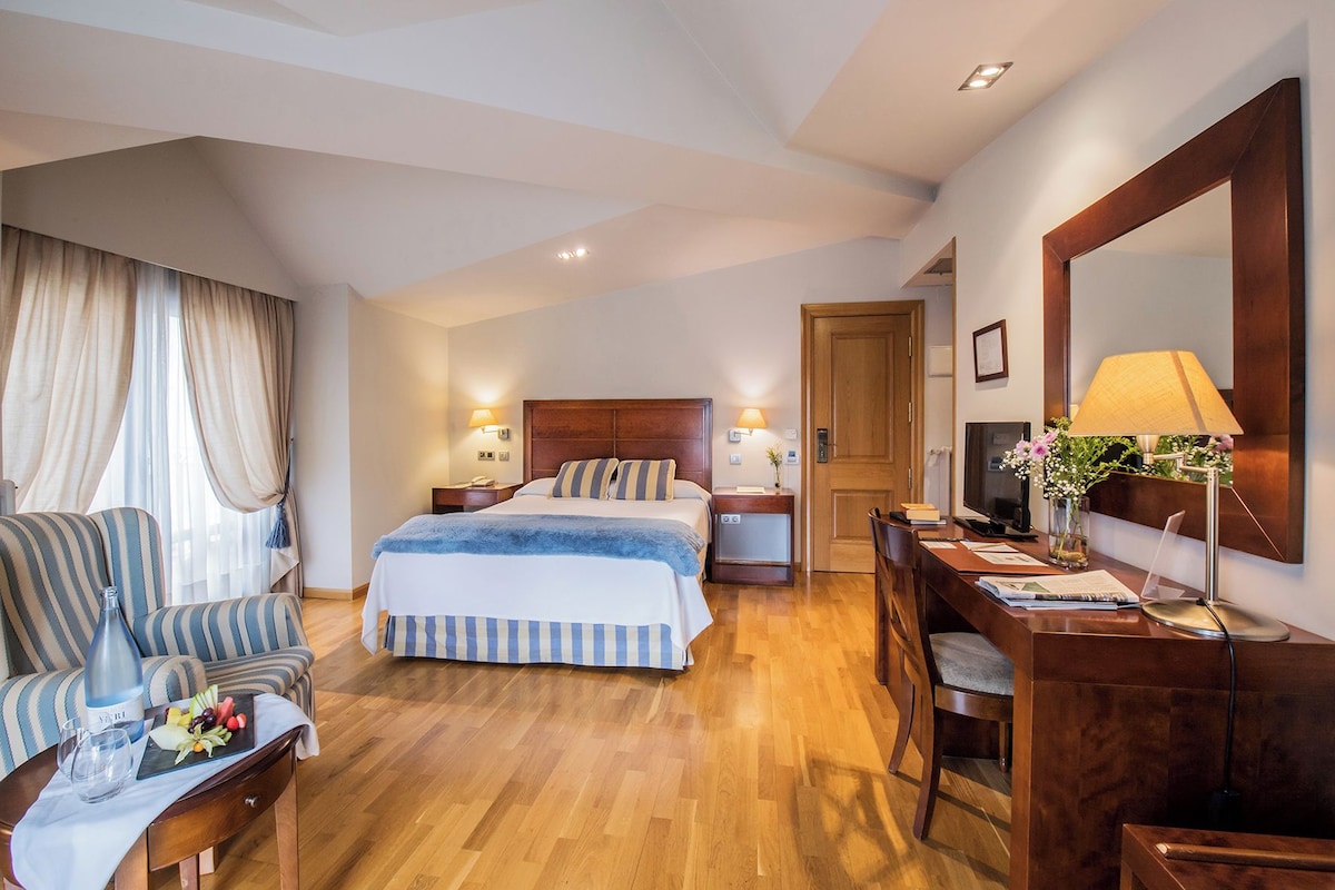 Una habitación de hotel con cama, escritorio, silla, televisor y lámpara.