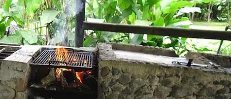 An outdoor grill with a stone wall backdrop, surrounded by lush greenery.