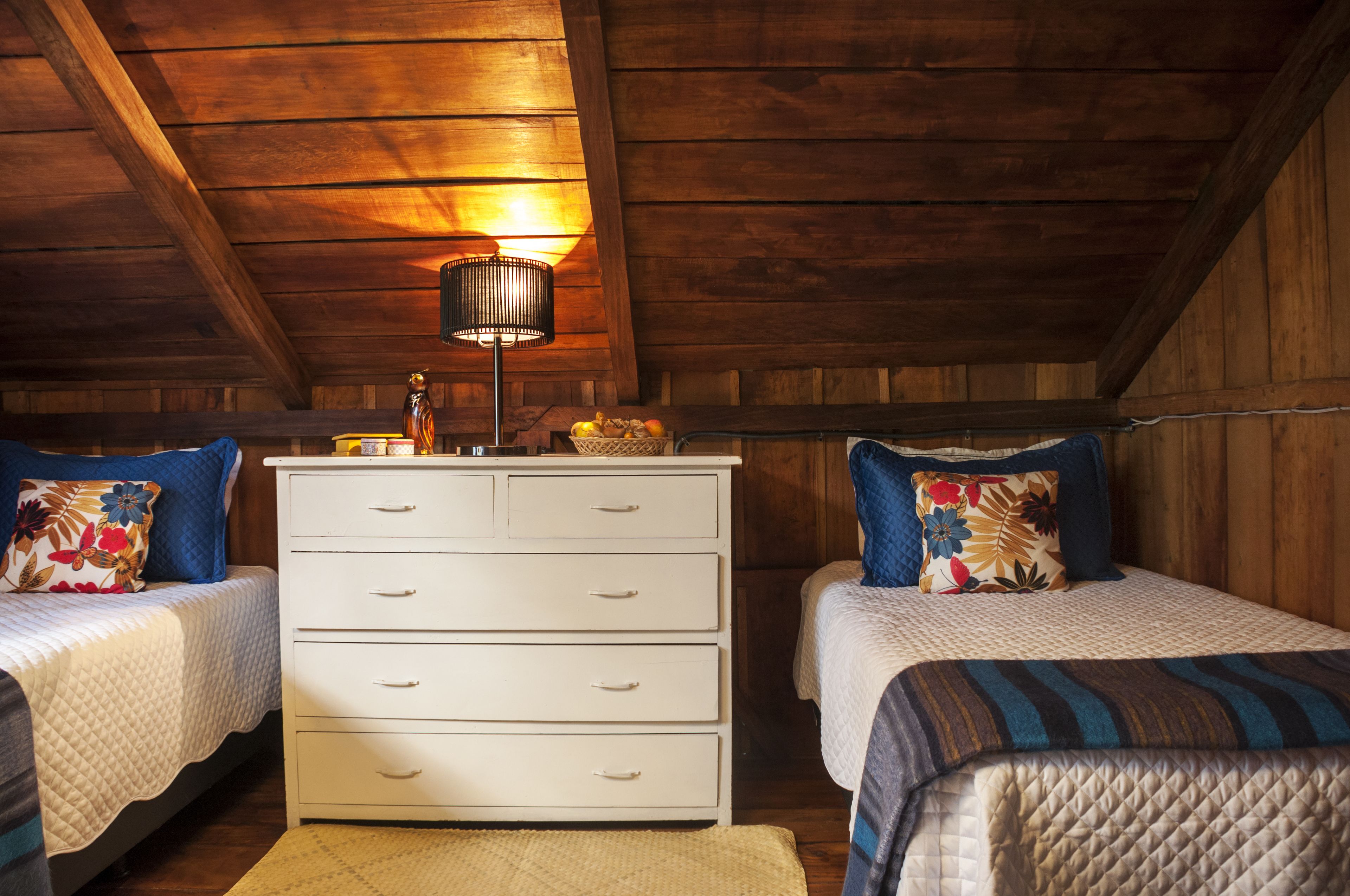 A cozy bedroom with two beds, a dresser, and a lamp.