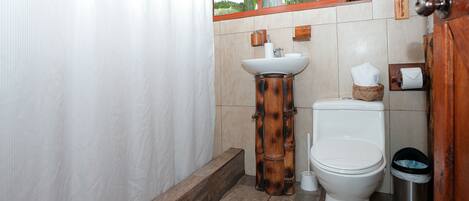 Un baño con lavamanos de pedestal de madera, un inodoro y un cubo de basura.