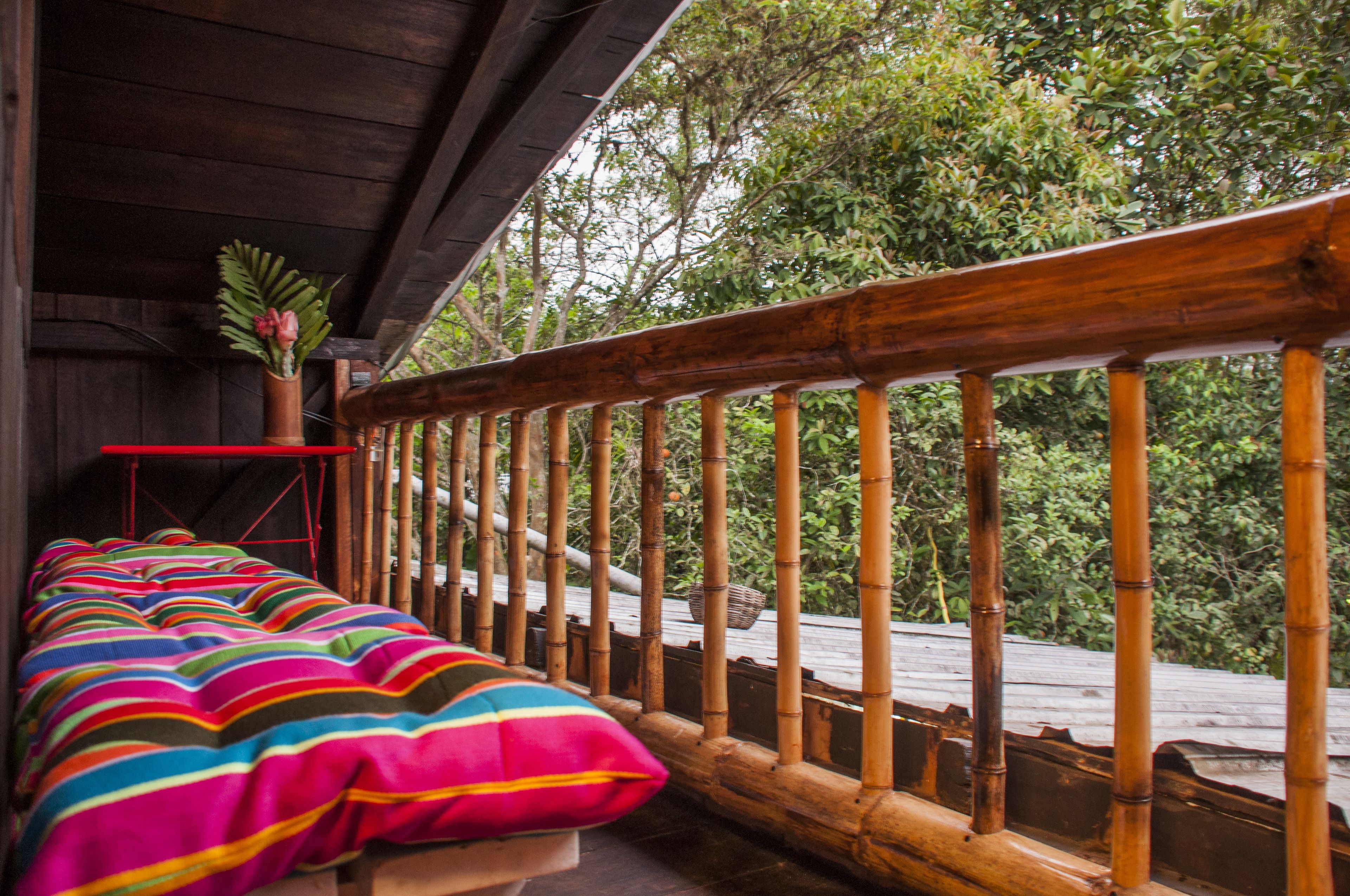 A wooden balcony with a bamboo railing, a colorful striped bed, and a potted plant.