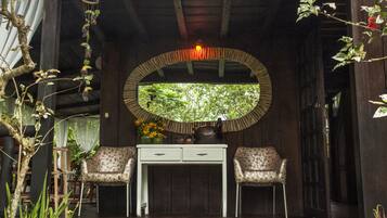 A room with a wooden ceiling, a round mirror, a white desk with two chairs, and a view of greenery through a window.