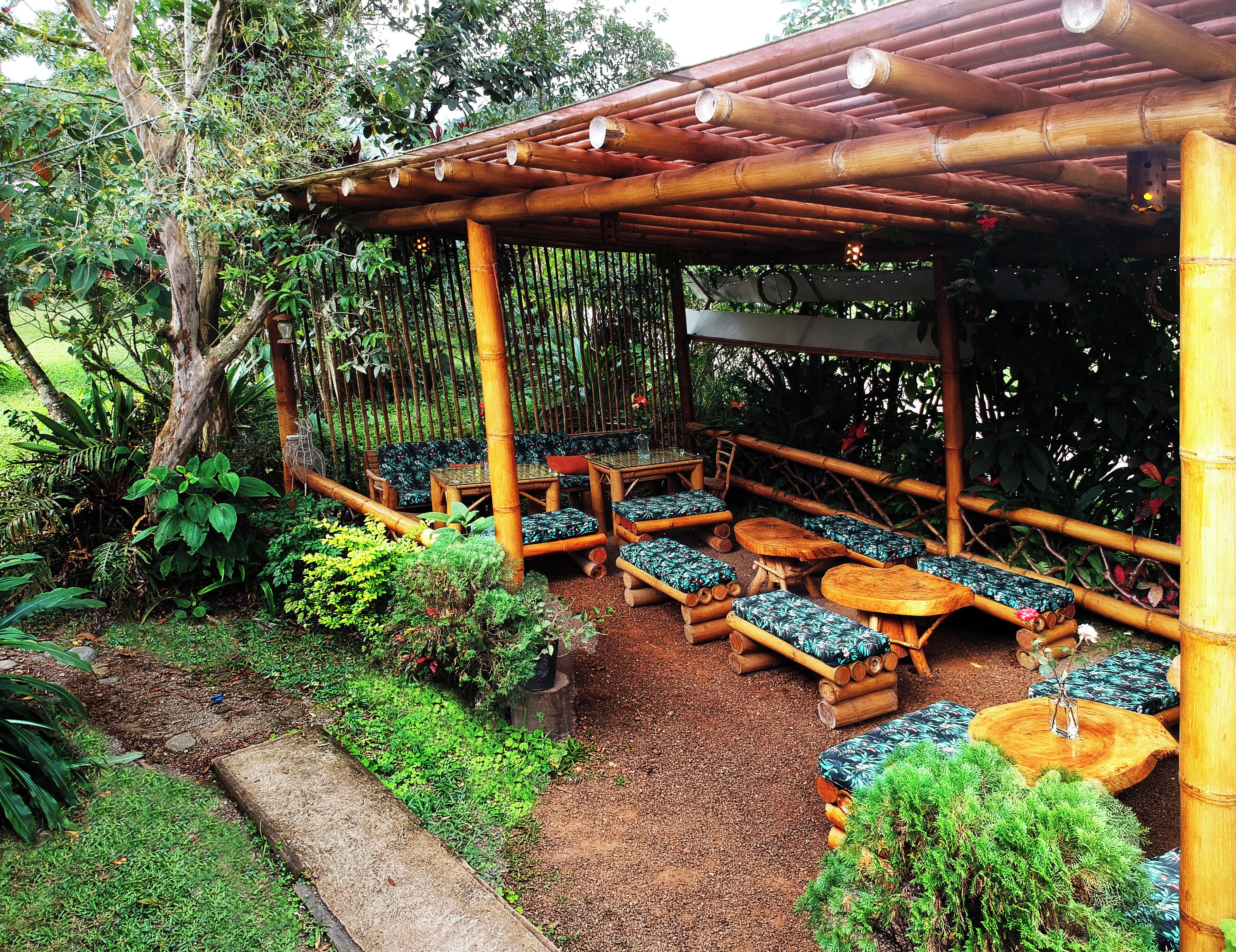 An outdoor seating area with bamboo furniture and a pergola structure, surrounded by lush greenery.