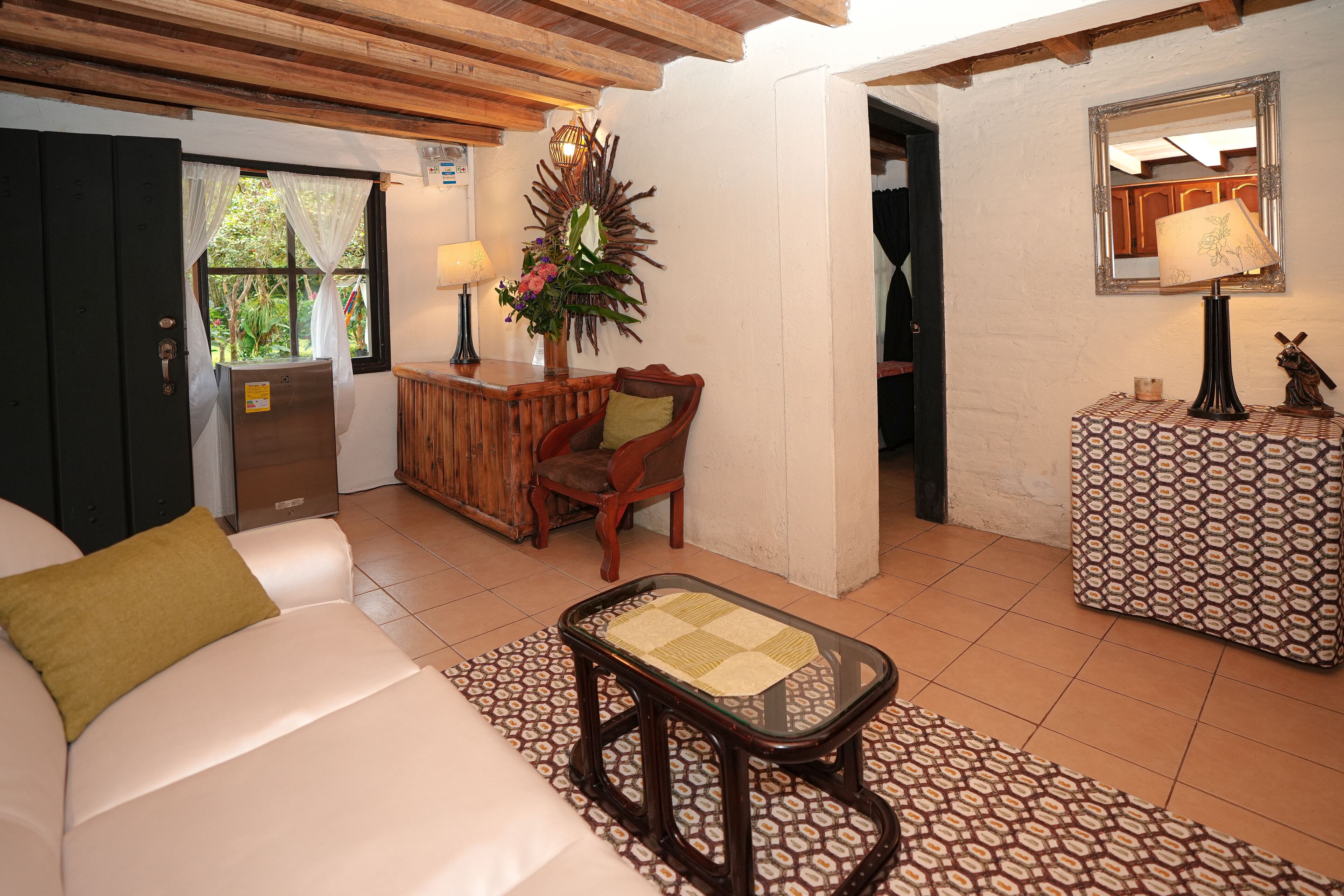A cozy living room with a sofa, a coffee table, a wooden chair, a side table with a lamp, and a decorative plant.