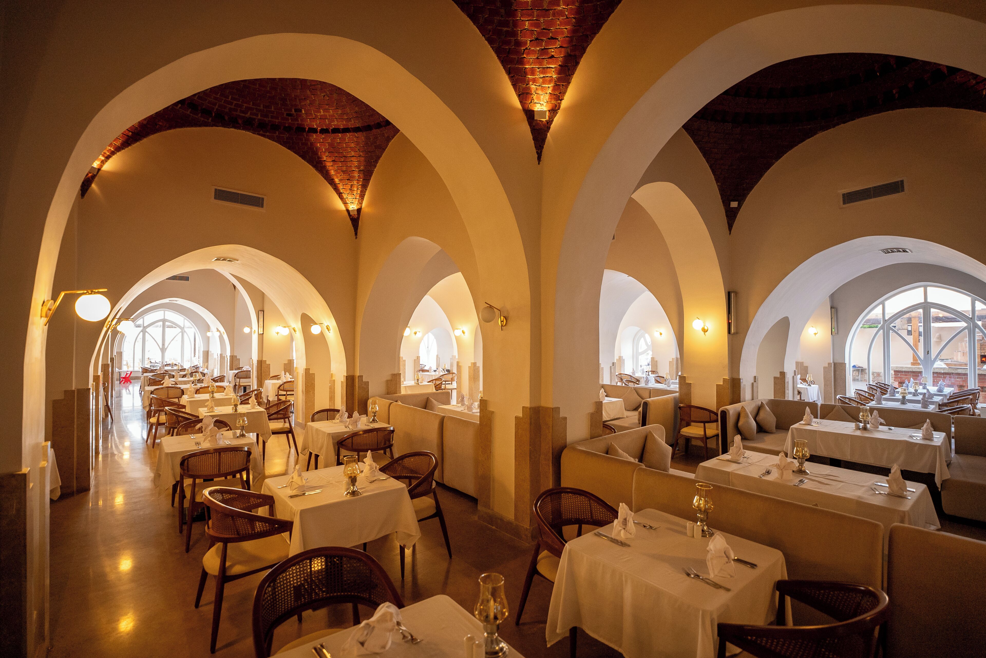 Un restaurante con varias zonas de comedor, cada una con mesas y sillas, y una pared de ladrillo al fondo.