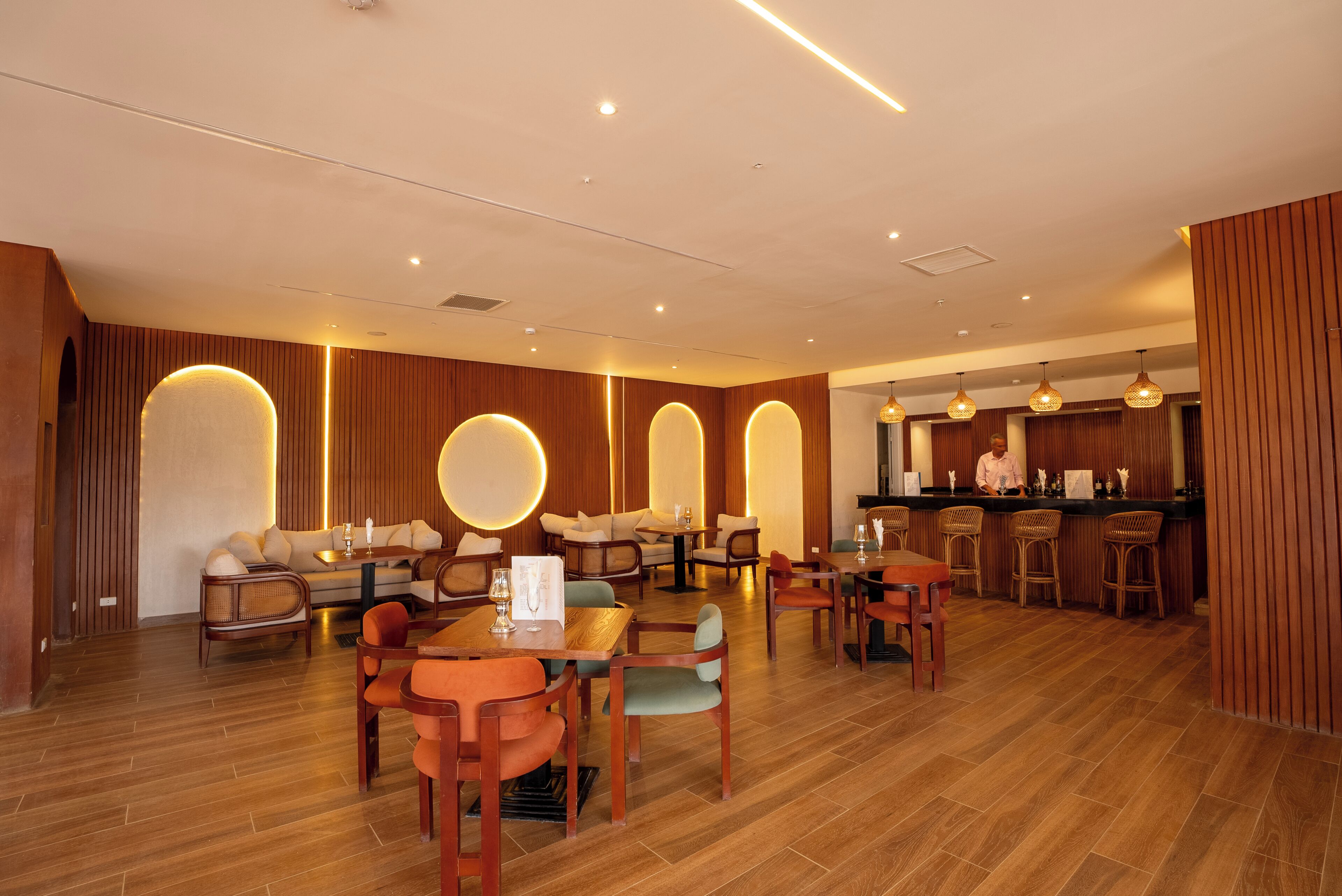 A modern restaurant interior with wooden paneling, round tables, and bar seating.