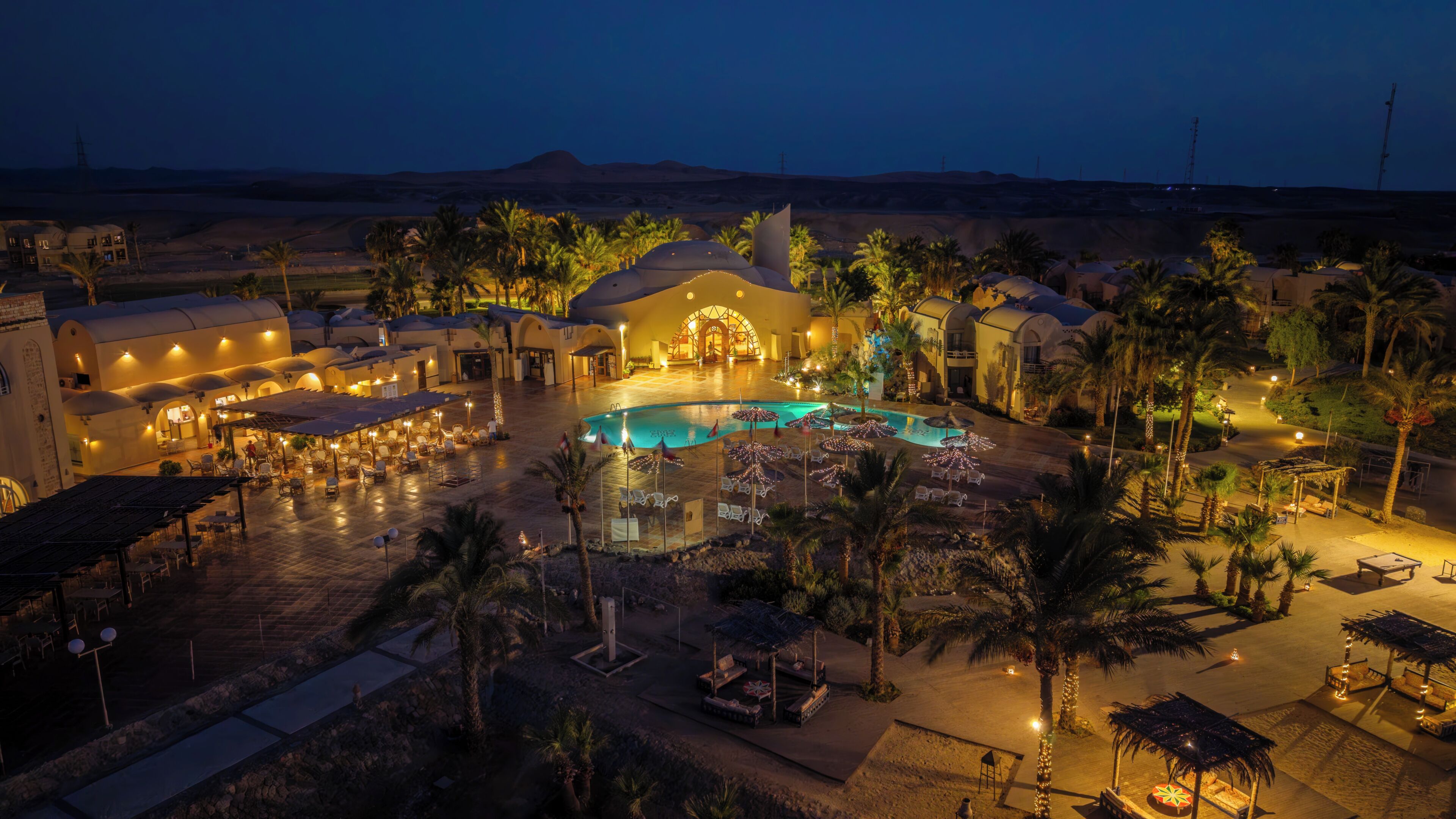 A resort with a swimming pool, palm trees, and a building with a dome-shaped entrance.