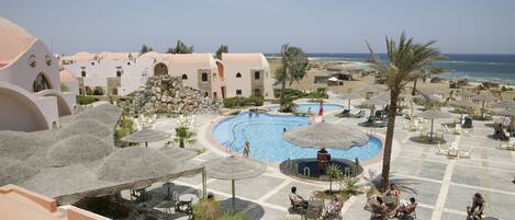 A resort with a central pool, outdoor seating, and a beach view.