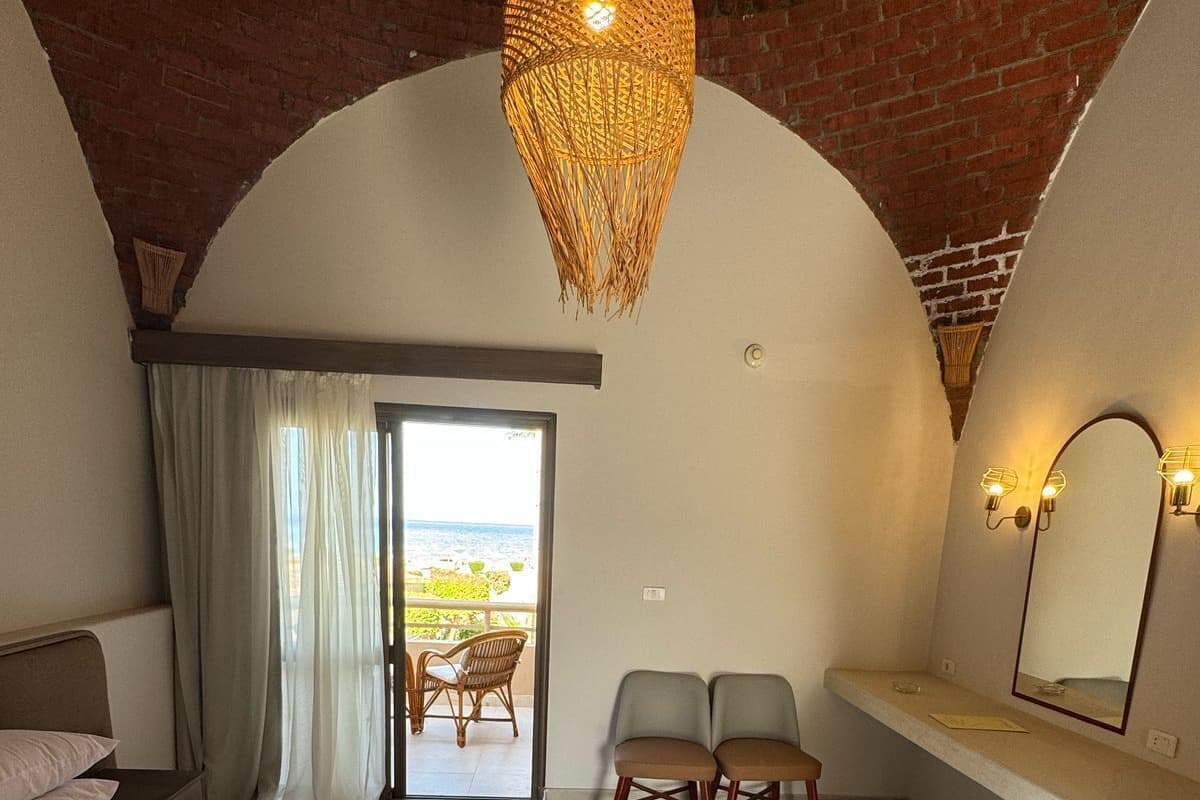 A bedroom with a large bed, a balcony with chairs, a hanging light fixture, and a mirror on the wall.