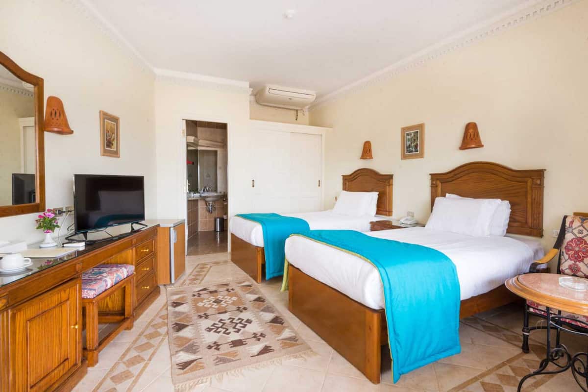 Quarto de hotel com duas camas, uma mesa de trabalho com televisão, banheiro e área de refeições.