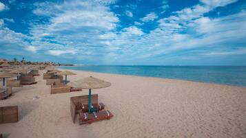 A beach with rows of sun loungers and umbrellas, a clear sky, and calm sea.