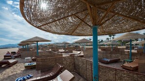 A beachside lounge area with wicker furniture and thatched umbrellas. - Shams Safaga Resort - All inclusive (Safaga)