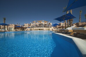 A swimming pool with lounge chairs and umbrellas, surrounded by buildings with balconies and palm trees. - Shams Prestige Abu Soma Resort - All inclusive (Safaga)