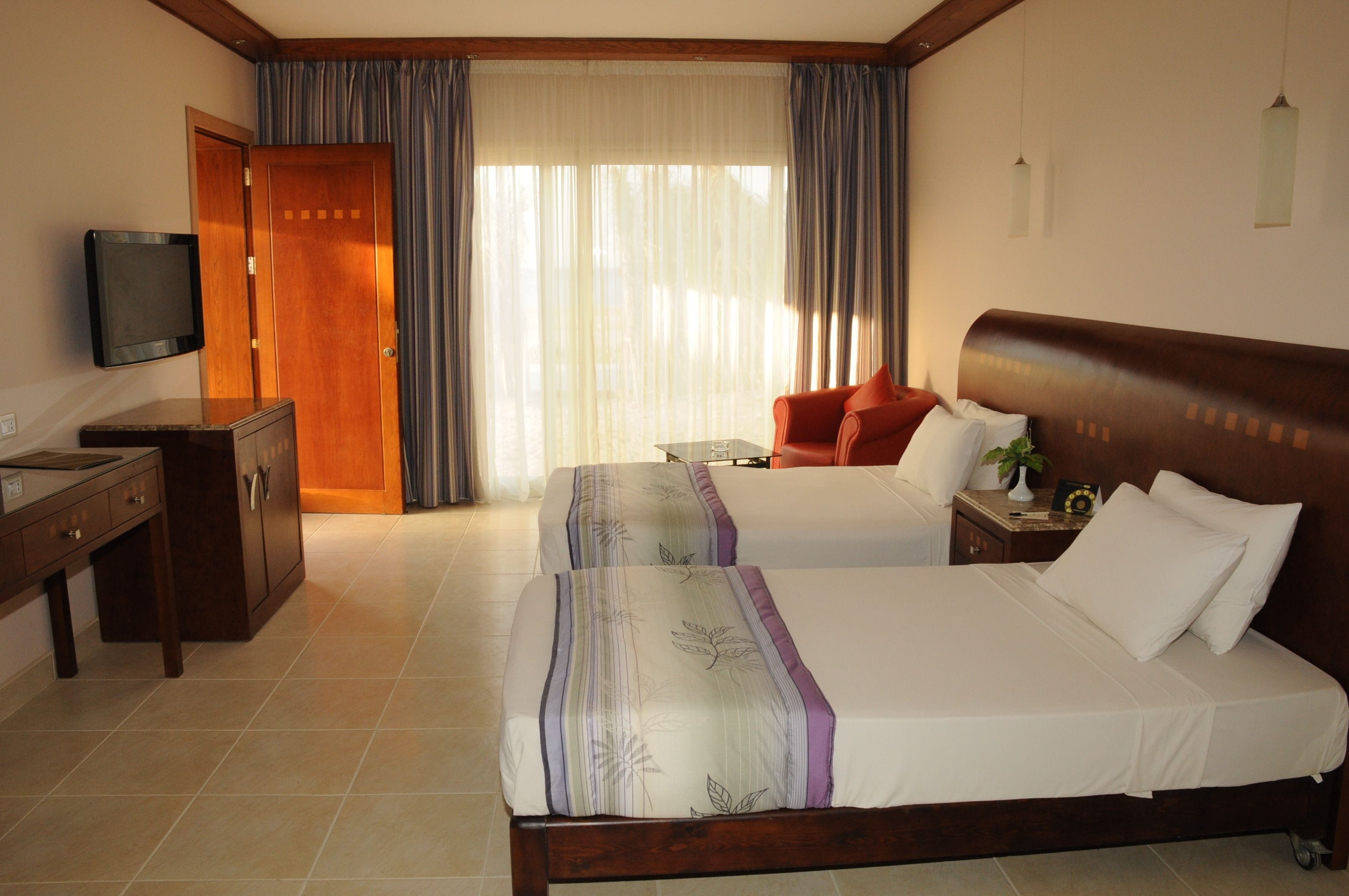 A hotel room with two beds, a desk, a television, and a window with curtains.