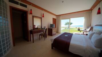 Habitación de hotel con cama, escritorio, silla, televisor y un ventanal con vista a la playa.