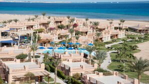 Un resort con varias edificaciones, un área de piscina con sombrillas y vista al mar.