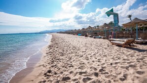 A beach with sun loungers and umbrellas, a clear sky, and a calm sea. - Imperial Shams Abu Soma - All inclusive (Safaga)