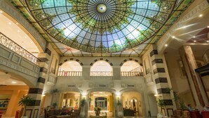 Een ruime lobby met een hoog, versierd glazen koepelplafond, meerdere zithoeken en een centrale decoratietafel.