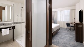 A hotel room with a shower, a bed, a desk, a chair, and a TV.