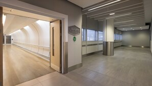 A modern hotel corridor with a curved ceiling, a Hampton by Hilton sign, and a view of the lobby through glass doors.