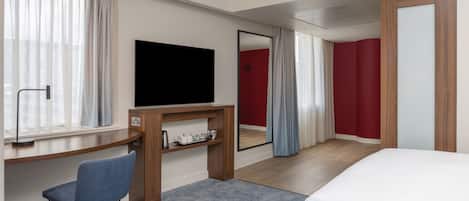 Una habitación de hotel con cama, escritorio, silla, televisor y espejo.