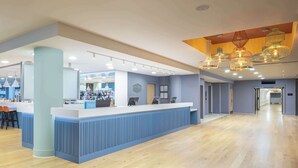 A modern hotel lobby with a reception desk, seating area, and a bar.