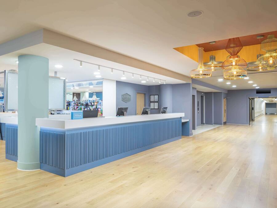 A modern hotel lobby with a reception desk, seating area, and a bar.