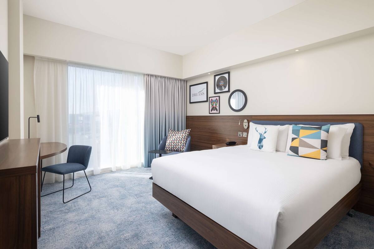 Une chambre d’hôtel avec un grand lit, un bureau, une chaise et une fenêtre avec des rideaux.