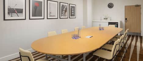 A conference room with a long table, chairs, framed artwork on the wall, a clock, and a door.
