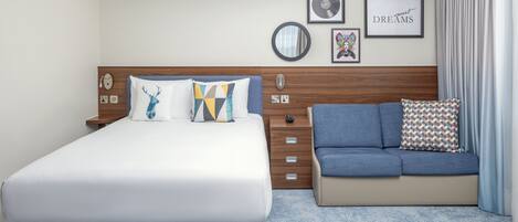 Quarto de hotel moderno com uma cama grande, um sofá, um encabimento de madeira e uma parede com obras de arte emolduradas e um espelho.