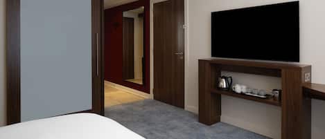 A hotel room with a bed, a TV on a wooden stand, a coffee maker, and a red door.
