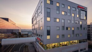 A modern hotel building with a prominent "Hampton" sign, multiple windows, and a glass facade.