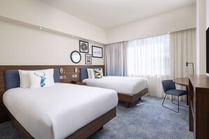Een hotelkamer met twee bedden, een bureau, een stoel en een groot raam met gordijnen.