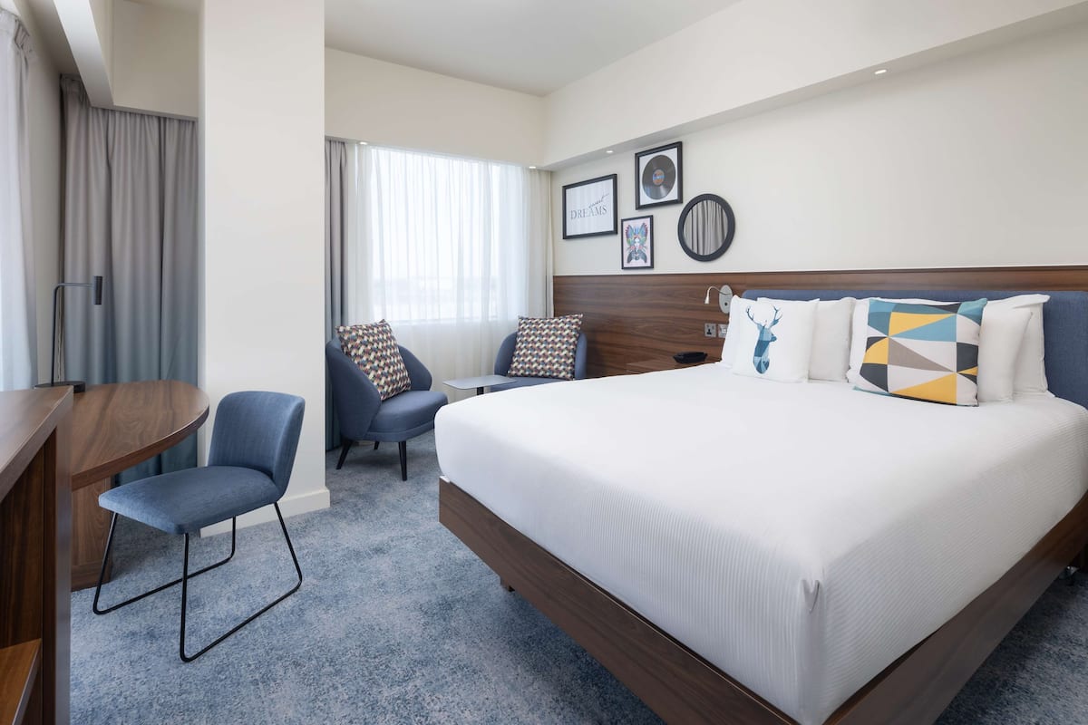 Une chambre d’hôtel avec un grand lit, un bureau, une chaise et une fenêtre avec des rideaux.