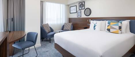 Een hotelkamer met een groot bed, een bureau, een stoel en een raam met gordijnen.