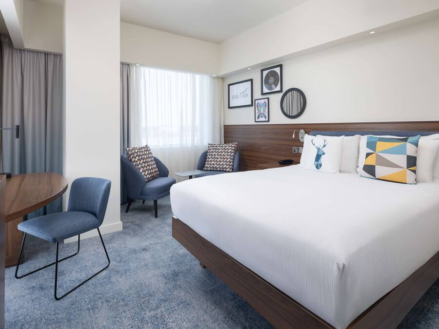 A hotel room with a large bed, a desk, a chair, and a window with curtains.