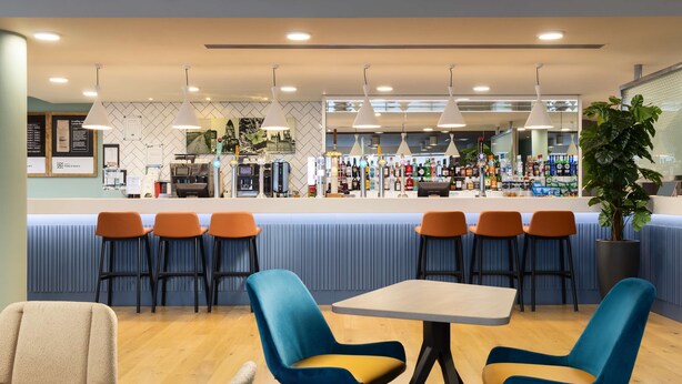 A modern bar area with a counter, multiple seating options including bar stools and cushioned chairs, and a variety of bottles and glasses on display.