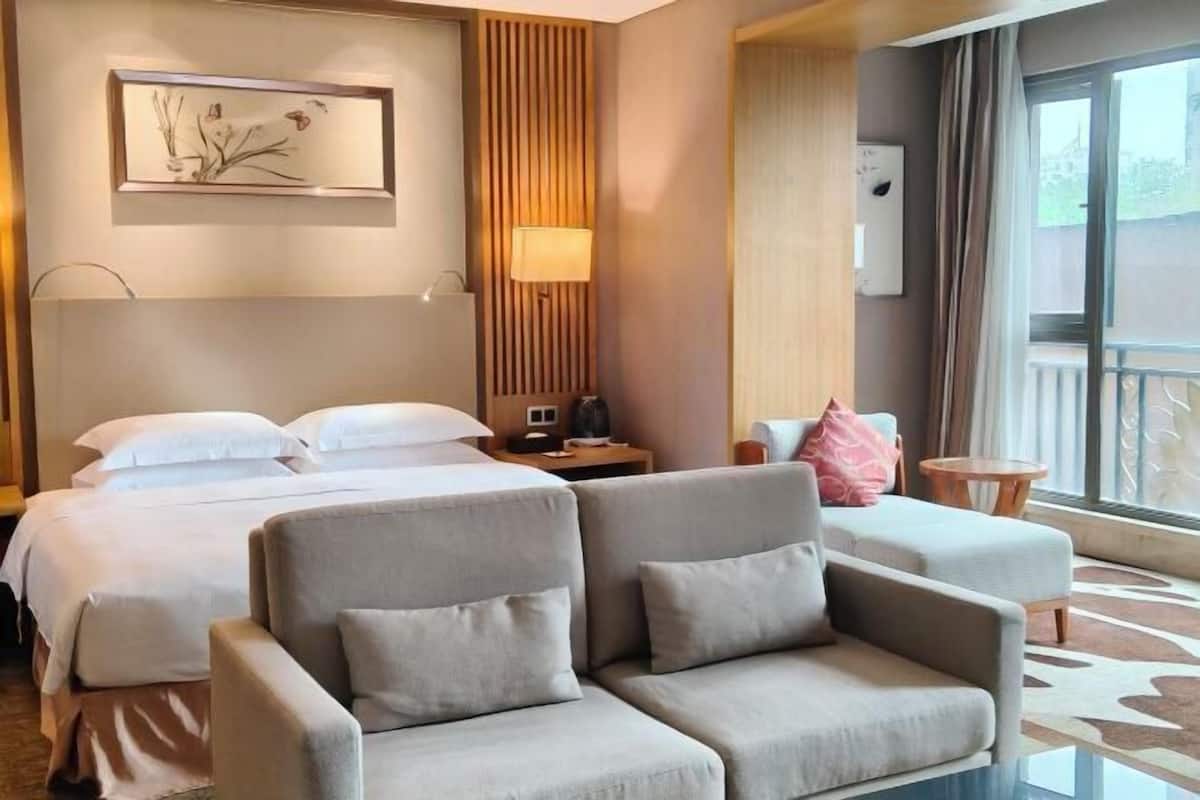 Ett hotellrum med en säng, två soffor, ett sängbord, en lampa, ett konstverk som hänger på väggen och ett fönster med gardiner.