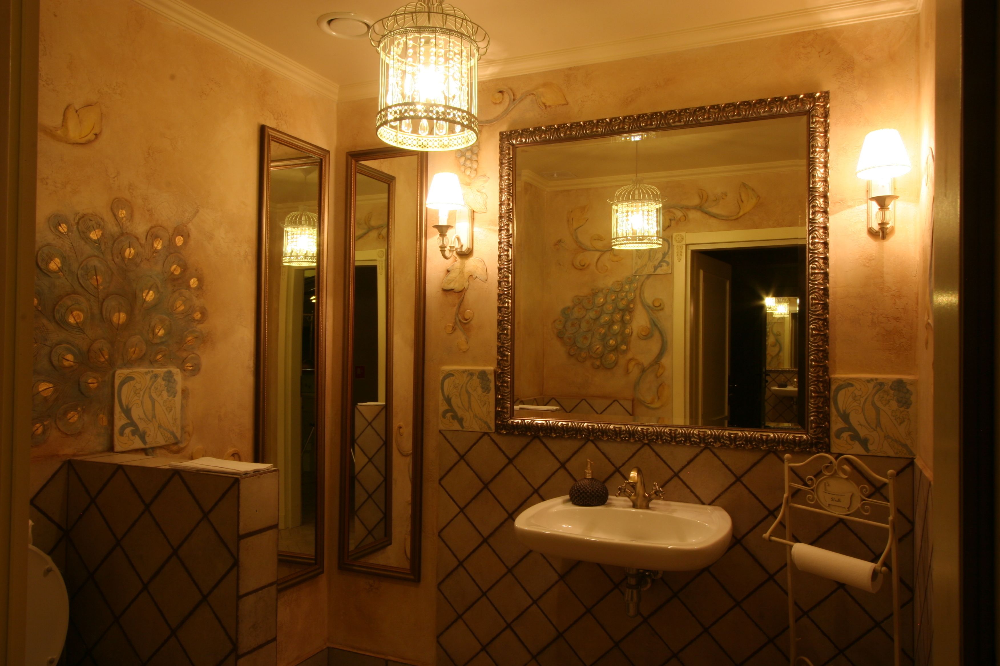 A bathroom with a large mirror, a sink, and a toilet. There are wall sconces and a chandelier.