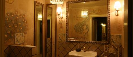 A bathroom with a large mirror, a sink, and a toilet. There are wall sconces and a chandelier.