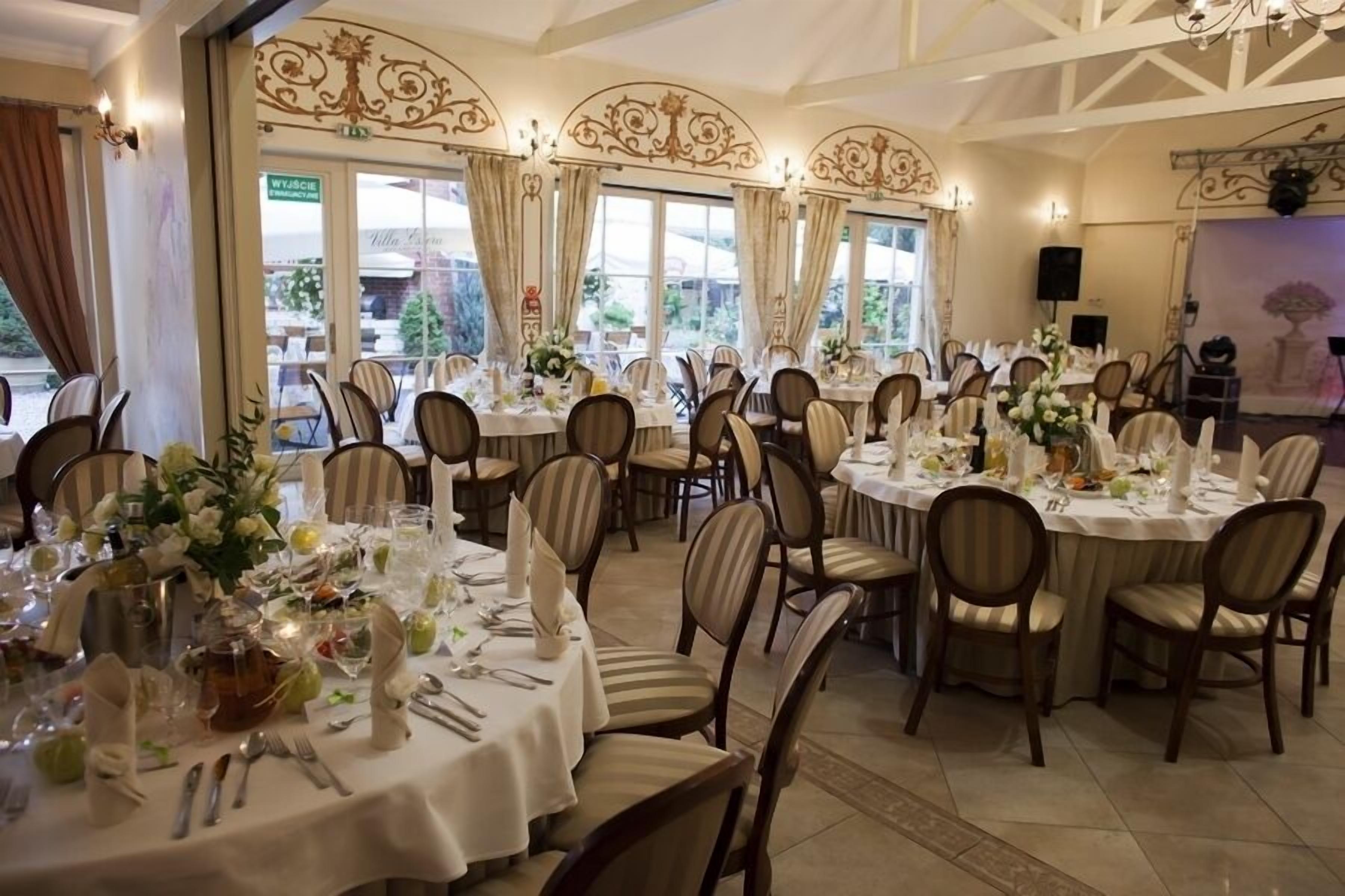 Un salón de banquetes con mesas redondas dispuestas para un evento formal, destacando una decoración elegante y sillas.