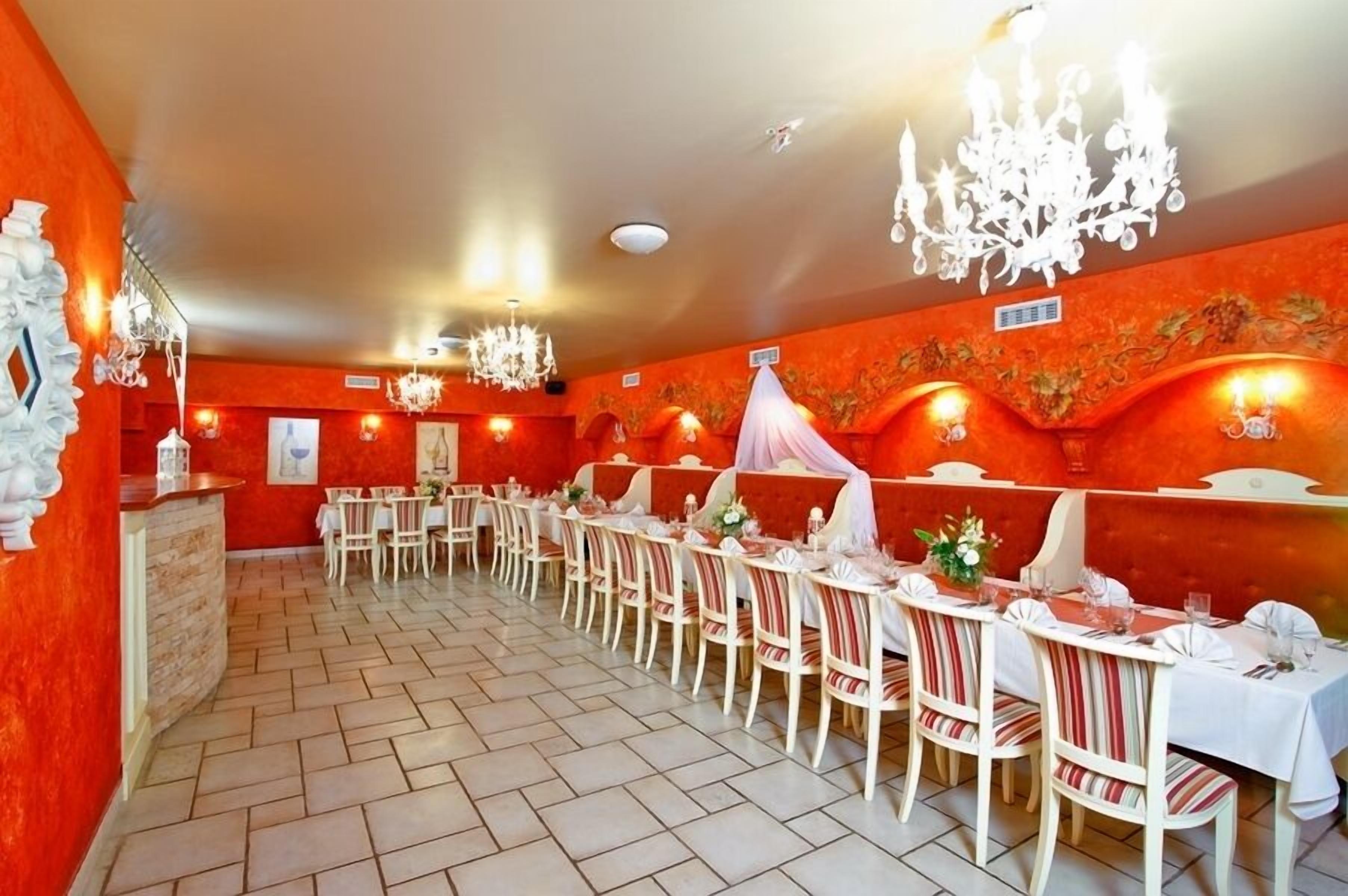 A restaurant with a long dining area, white chairs, and tables set with white tablecloths and candles.