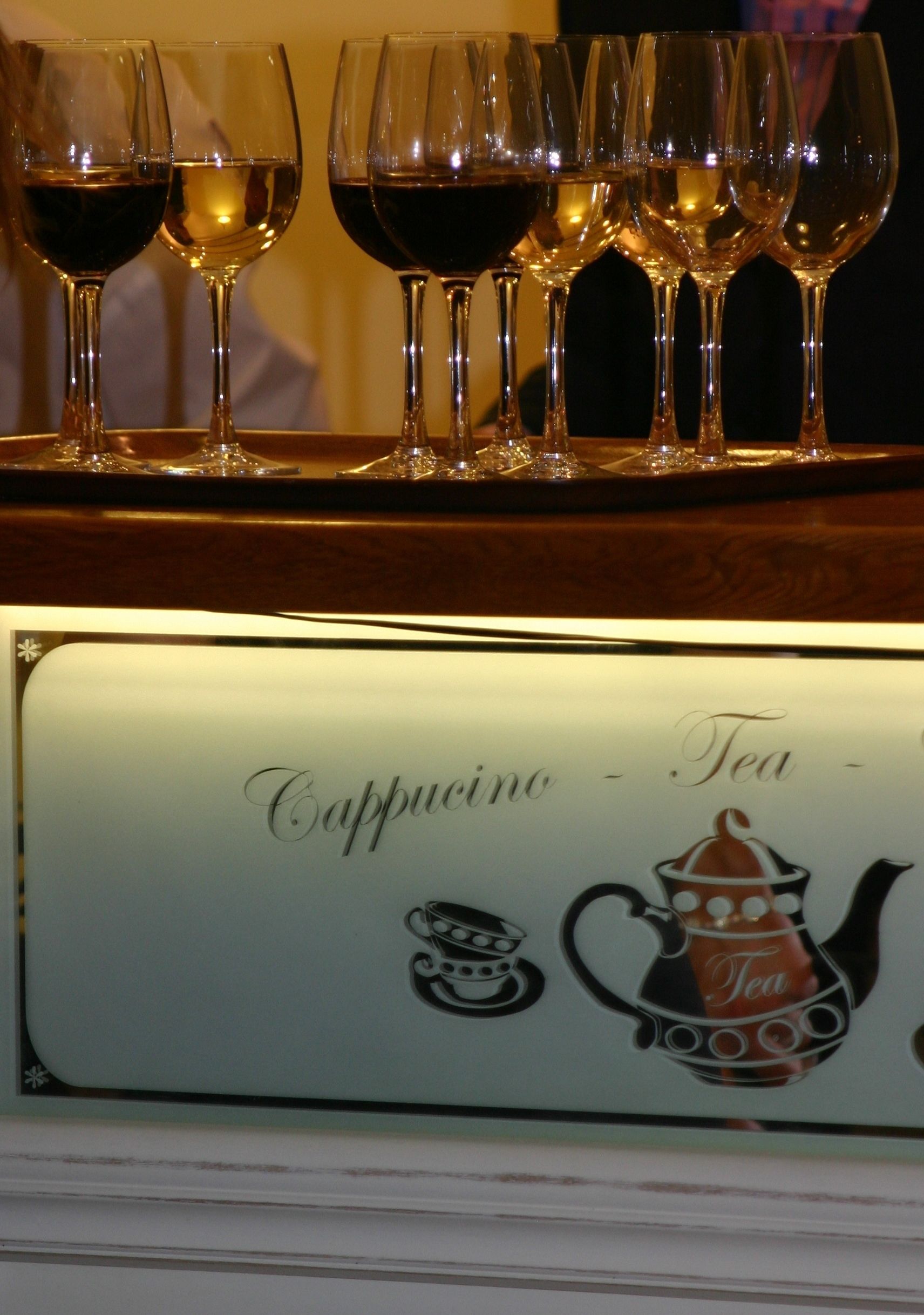 Una hilera de copas de vino sobre una estantería con un cartel que dice "Cappuccino - Té".
