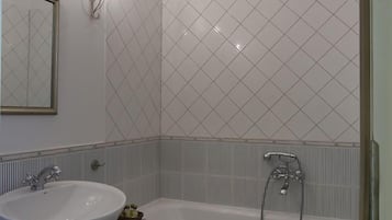 A bathroom with a white sink, a bathtub, and a shower. There is a towel hanging on the wall.