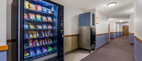 A hallway with a vending machine stocked with snacks and a refrigerator.