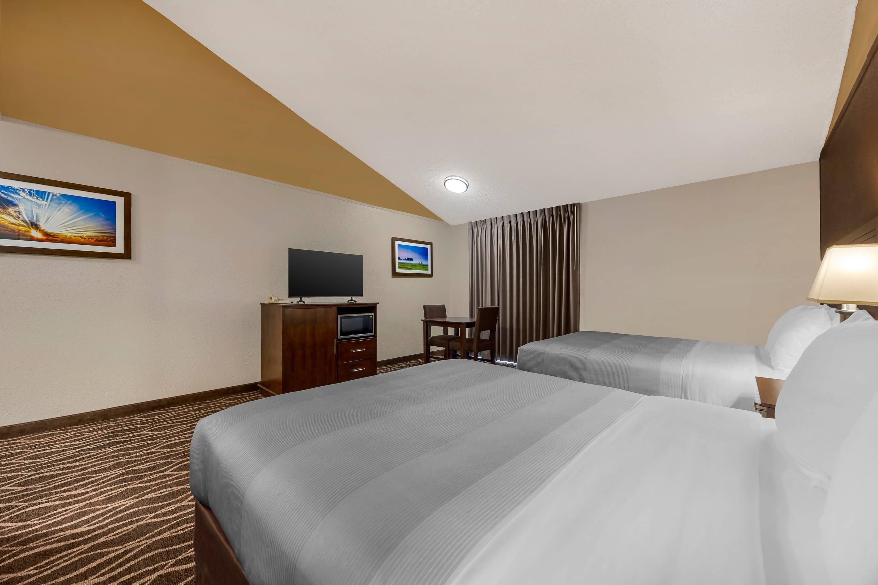 A hotel room with two beds, a desk with a chair, a TV, and a window with curtains.