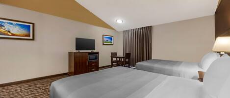 A hotel room with two beds, a desk with a chair, a TV, and a window with curtains.